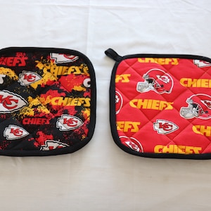 May include: Two square pot holders with black trim. One is black with red and yellow accents, the other is red. Both feature the words "CHIEFS" and the team logo.