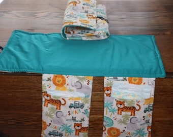 May include: A baby changing station with a teal changing pad and a roll-up diaper clutch. The clutch and pockets feature a safari animal print with lions, tigers, and elephants. The changing pad is rectangular.