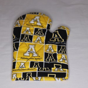 May include: A quilted oven mitt featuring a repeating pattern of black and gold squares with the letter "A" and the words "Appalachian State". The mitt is designed for kitchen use.