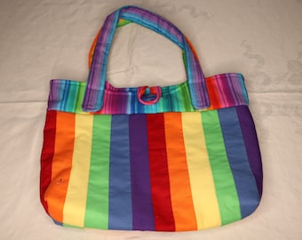 May include: A colorful tote bag with a rainbow striped design. The bag features vertical stripes in red, orange, yellow, green, blue, and purple. It has matching rainbow handles and a button closure. The bag is made of fabric.