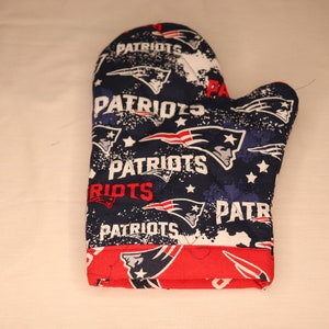 May include: A quilted oven mitt featuring a navy blue, white, and red Patriots design. The mitt displays the team's logo and the word "PATRIOTS" in white and red. The cuff is red.