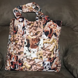 May include: A tote bag featuring a patchwork design of various dog breeds and dog bone shapes. The bag has a rectangular shape with a handle made from the same fabric. The color palette includes browns, tans, and whites.