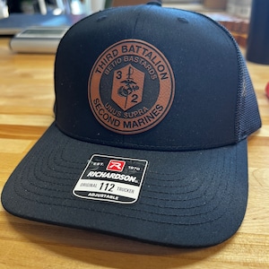May include: Black trucker hat with a brown leather patch that says "Third Battalion Betio Bastards Unus Supra Second Marines". The hat also has a red "R" logo and the text "Richardson Original 112 Trucker Adjustable".