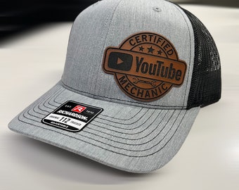 May include: A gray and black trucker hat with a brown leather patch that says "Certified YouTube Mechanic".