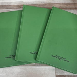May include: Three green hardcover books with the text "7530-00-222-3521 FEDERAL SUPPLY SERVICE" printed on the lower right corner. The books are arranged in a slightly overlapping pattern on a wooden surface.