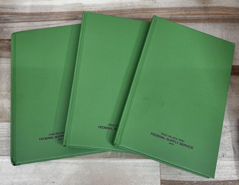 May include: Three green hardcover books with the text "7530-00-222-3521 FEDERAL SUPPLY SERVICE" printed on the lower right corner. The books are arranged in a slightly overlapping pattern on a wooden surface.
