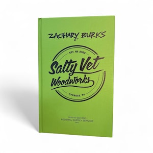 May include: A lime green book with the text "ZACHARY BURKS" at the top. Below is a circular logo that reads "Salty Vet Woodworks" with "EST. 2022" above and "CYPRESS, TX" below. The bottom of the book has the text "FEDERAL SUPPLY SERVICE".
