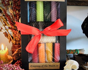 May include: A black box of 14 mini beeswax spell candles tied with a red ribbon. The candles are in various colors, including blue, green, and red. The box has the text "14 Mini Beeswax Spell Candles" and "Empress of the Moon.co".