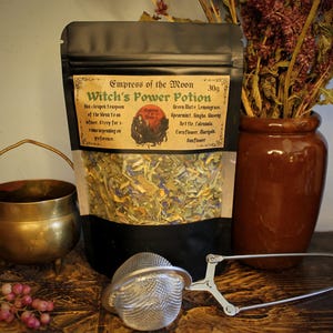 May include: A black pouch with a label that reads "Empress of the Moon Witch's Power Potion 30g". The label lists the ingredients: Green Mate, Lemongrass, Spearmint, Ginger, Nettle, Calendula, Cornflower, Marigold, Sunflower. The pouch contains a blend of dried herbs.