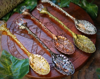 May include: Five ornate spoons with crystal handles. The spoons are made of different metals, including gold, silver, and copper. Each spoon has a unique floral design.