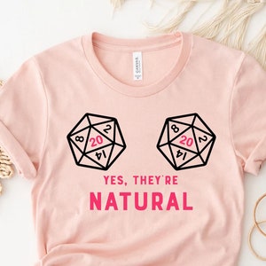May include: Pink t-shirt with a graphic of two dice with the number 20 showing on each die. The text "YES, THEY'RE NATURAL" is printed below the dice.