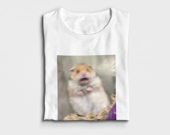 May include: A white t-shirt with a printed image of a hamster with a surprised expression. The hamster is brown and white and is standing on a bed of shredded paper.