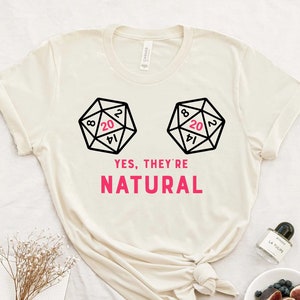 Puede incluir: Una camiseta blanca con un gráfico de dos dados con el número 20 mostrando. El texto "YES, THEY'RE NATURAL" está impreso debajo de los dados.