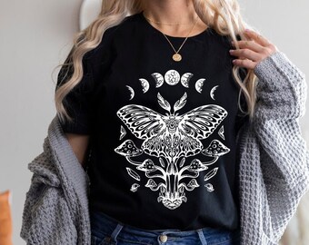 Puede incluir: Camiseta negra con un diseño gráfico blanco de una polilla con las alas extendidas, rodeada de setas y un diseño de fase lunar creciente.