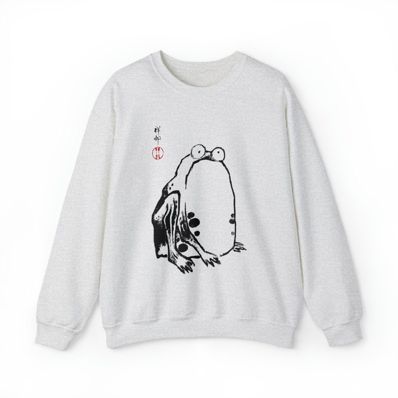 May include: A light gray sweatshirt with a black and white illustration of a frog on the front. The frog is sitting on its hind legs with its front legs outstretched. The illustration is in a Japanese style and includes the Japanese characters "蛙" (frog) and a red circle.