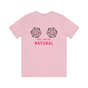 May include: Pink t-shirt with a graphic of two dice with the number 20 on the top face. The text "YES, THEY'RE NATURAL" is printed below the dice.