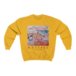 May include: Mustard yellow sweatshirt with a print of a Matisse painting depicting a coastal scene. The print includes the text "MATISSE View of Collioure". The sweatshirt has a crew neck and long sleeves.