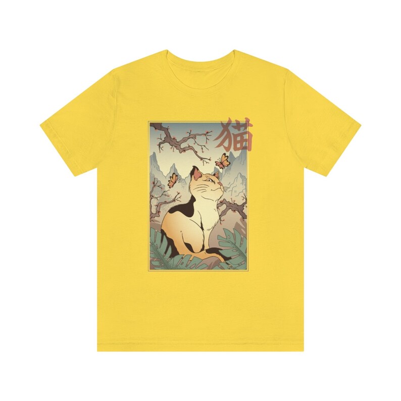 May include: Yellow t-shirt with a graphic of a cat sitting in a Japanese garden with butterflies and the word "猫" (cat in Japanese) in red.