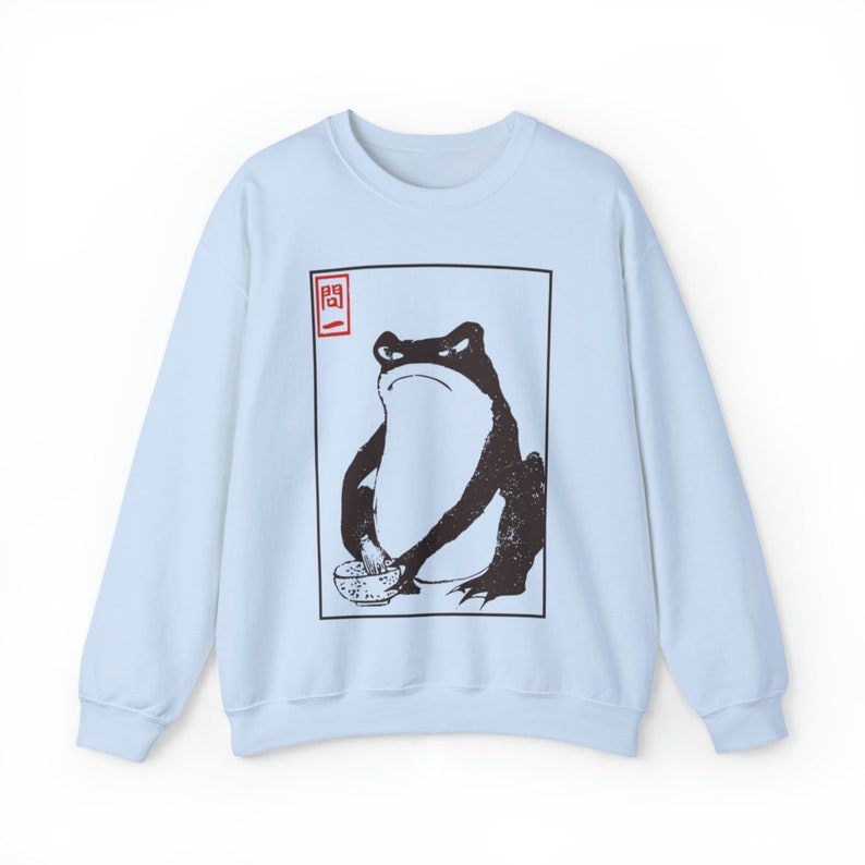 May include: Light blue sweatshirt with a black and white illustration of a frog holding a bowl. The illustration is framed in a black square with a red square in the top left corner that contains a Japanese character.