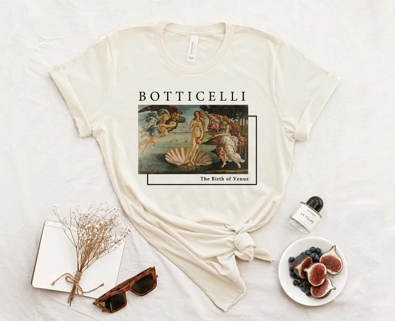 May include: A beige t-shirt with a graphic print of Sandro Botticelli's "The Birth of Venus" painting. The text "Botticelli" and "The Birth of Venus" is printed below the image.