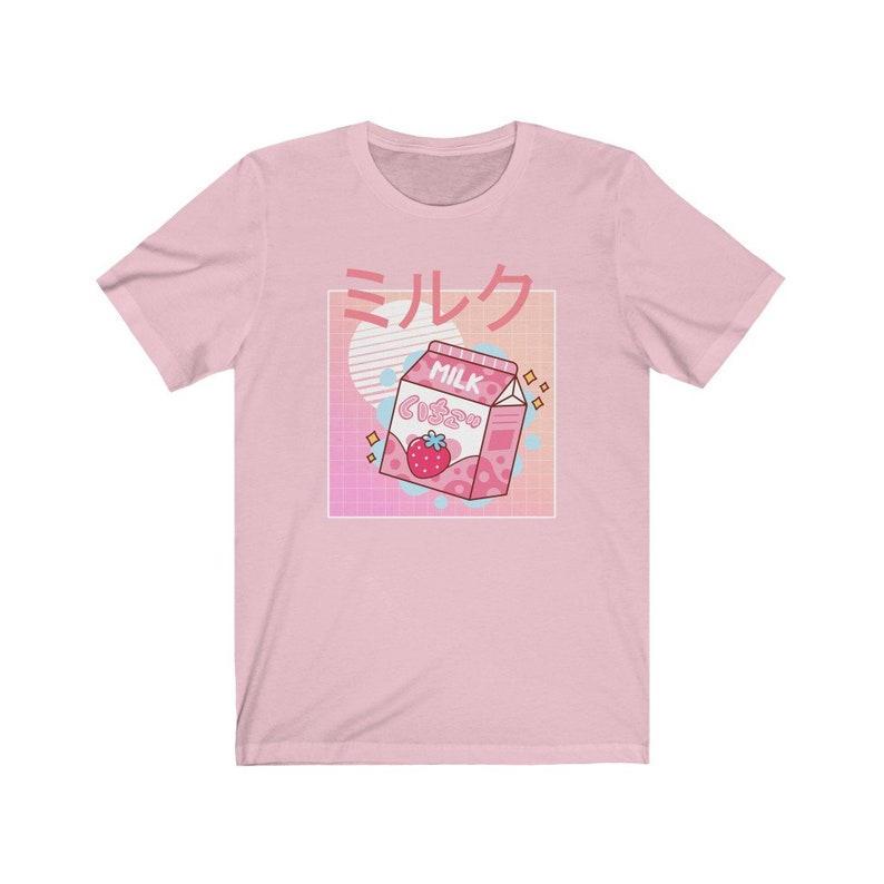 Op de afbeelding: Lichtroze t-shirt met een afbeelding van een roze aardbeienmelkpak en Japanse tekst. Het ontwerp bevat een witte vierkant, een roze en blauwe gradi&euml;nt en een witte cirkel.