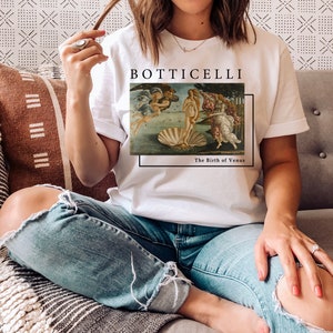 May include: White t-shirt with a graphic of Sandro Botticelli's "The Birth of Venus" painting. The text "Botticelli" and "The Birth of Venus" are printed below the image.