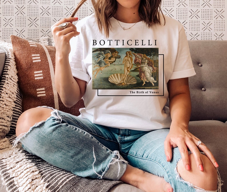May include: White t-shirt with a graphic of Sandro Botticelli's "The Birth of Venus" painting. The text "Botticelli" and "The Birth of Venus" are printed below the image.