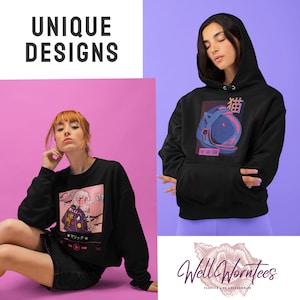 May include: Two models are wearing black sweatshirts with unique graphic designs. The first sweatshirt features a pink and white anime-style illustration of a girl with a cherry blossom background. The second sweatshirt features a blue and pink illustration of a cat wearing a space helmet with Japanese text. Both sweatshirts have the text "Well Worntees" on the bottom.