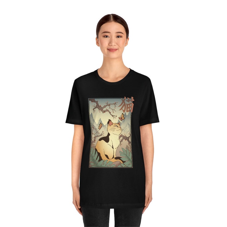 May include: Black t-shirt with a graphic print of a cat sitting in a forest scene with butterflies. The Japanese word for cat, "猫" (Neko), is printed in the top right corner of the graphic.