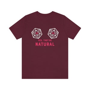 May include: A maroon t-shirt with a white graphic of two twenty-sided dice, with the text "YES, THEY'RE NATURAL" in pink.