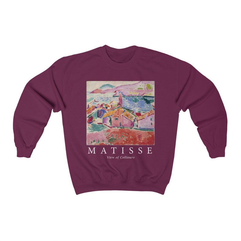 May include: A maroon sweatshirt with a print of a Matisse painting of a coastal scene. The artwork shows buildings with red roofs, the sea, and the text "MATISSE View of Collioure" in white.