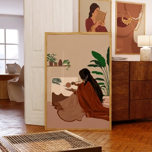 May include: A digital art print featuring a woman in a red and beige outfit painting in front of a window with plants. The print has a minimalist style and is framed in a light wood frame.