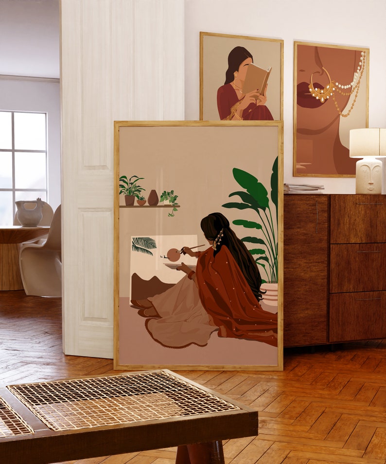 May include: A digital art print featuring a woman in a red and beige outfit painting in front of a window with plants. The print has a minimalist style and is framed in a light wood frame.