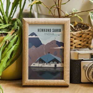 May include: A framed print of a colorful illustration depicting a building with a blue roof and a mountain range in the background. The text "Hemkund Sahib, India" is printed at the top of the print.