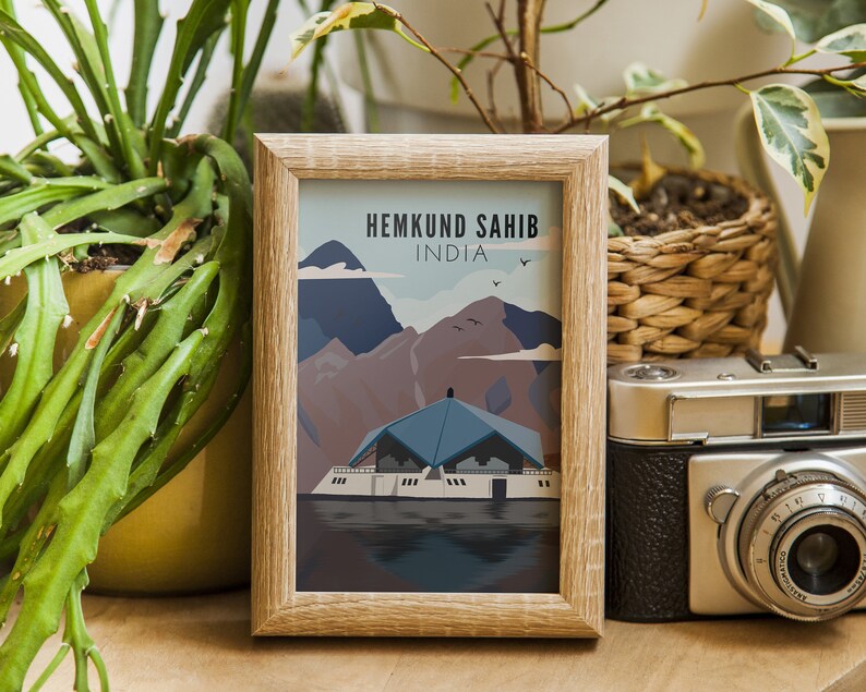 May include: A framed print of a colorful illustration depicting a building with a blue roof and a mountain range in the background. The text "Hemkund Sahib, India" is printed at the top of the print.