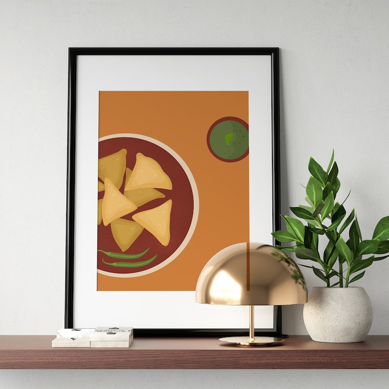May include: A framed print of a plate of samosas with green chutney on a brown background. The print is on a shelf with a gold lamp and a potted plant.
