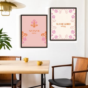 May include: Two framed prints with pink floral borders and orange text. The left print has a pink background and says "Satnam" in orange text. The right print has a white background and says "Waheguru" in orange text with a Gurmukhi script underneath.