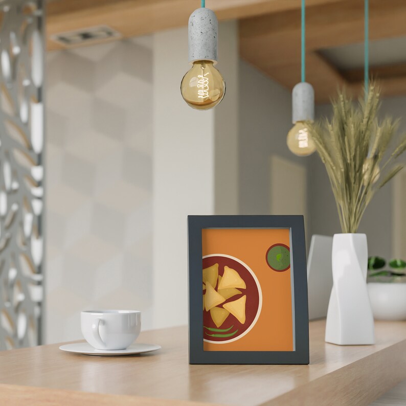 May include: A framed illustration of a plate of samosas with a side of green chutney. The illustration is on a light orange background with a dark brown frame.
