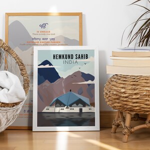 May include: A white framed print with a blue and brown illustration of a building with mountains in the background. The text "Hemkund Sahib India" is at the top of the print.