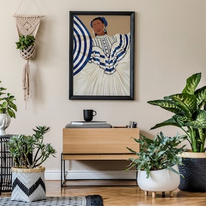 May include: A framed illustration of a woman wearing a blue and white striped dress with a blue headband. The illustration is hanging on a beige wall above a wooden shelf with a black mug, books, and a potted plant.