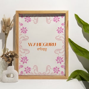 May include: A framed print with a floral design and the text "WAHEGURU ਵਾਹਿਗੁਰੂ" in orange and black. The frame is made of light wood and has a white background.
