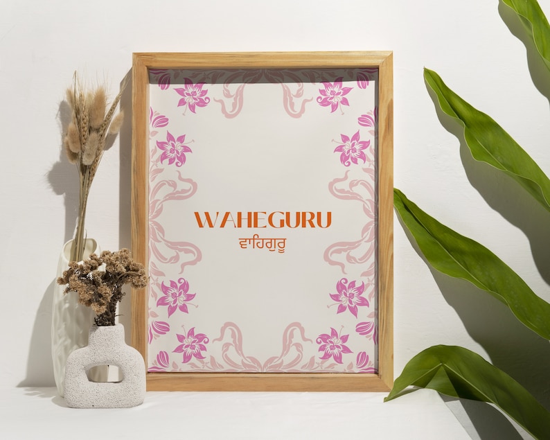 May include: A framed print with a floral design and the text "WAHEGURU ਵਾਹਿਗੁਰੂ" in orange and black. The frame is made of light wood and has a white background.