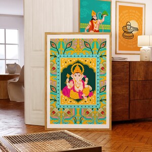 Może przedstawiać: Oprawiony wydruk hinduskiego b&oacute;stwa Ganesha, przedstawiony w żywych kolorach, dominuje na pierwszym planie. Dwa inne oprawione wydruki, z hinduskimi obrazami, są widoczne w tle. Grafika jest wystawiona w dobrze oświetlonym pomieszczeniu z drewnianymi meblami i podłogami.
