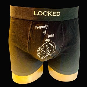 Peut inclure: Boxer noir avec le texte "LOCKED" sur la ceinture et "Property of Julia" avec un graphique de deux anneaux entrelacés sur le devant.