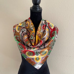 Pu&ograve; includere: Una sciarpa paisley colorata nei toni del marrone, oro, rosso e verde. La sciarpa quadrata &egrave; drappeggiata su un manichino nero, mettendo in risalto il suo motivo intricato e i colori vivaci. Il design della sciarpa presenta un motivo floreale ripetuto.