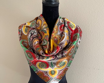 May include: A colorful paisley scarf in shades of brown, gold, red, and green. The square scarf is draped over a black mannequin, showcasing its intricate pattern and vibrant colors. The scarf's design features a repeating floral motif.