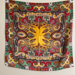 Pu&ograve; includere: Una sciarpa quadrata decorativa con un vivace motivo paisley. La sciarpa presenta un centro giallo con un design dettagliato in rosso, verde, marrone e bianco. Il bordo ha un motivo ripetitivo di rosso, verde e bianco.