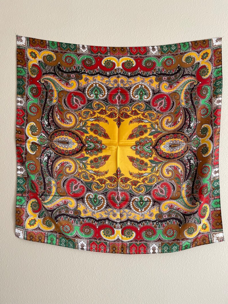 Pu&ograve; includere: Una sciarpa quadrata decorativa con un vivace motivo paisley. La sciarpa presenta un centro giallo con un design dettagliato in rosso, verde, marrone e bianco. Il bordo ha un motivo ripetitivo di rosso, verde e bianco.