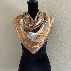 May include: A brown silk scarf with a white and gold pattern of chains and nautical knots. The scarf is folded and displayed on a black mannequin.