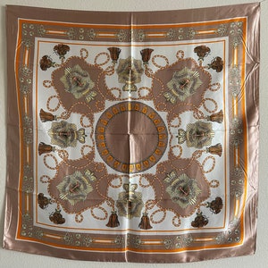 May include: A square silk scarf with a brown background and a white center. The center features a repeating pattern of gold rope, tassels, and a stylized design. The scarf has a gold and orange border.